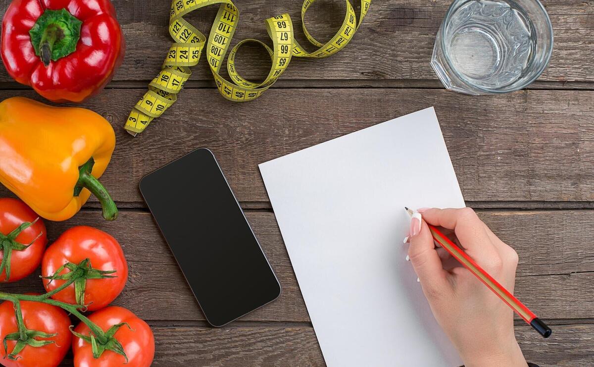 Concept diet, slimming plan with vegetables top view mock up. A female hand in a sports bracelet writes an article about proper nutrition